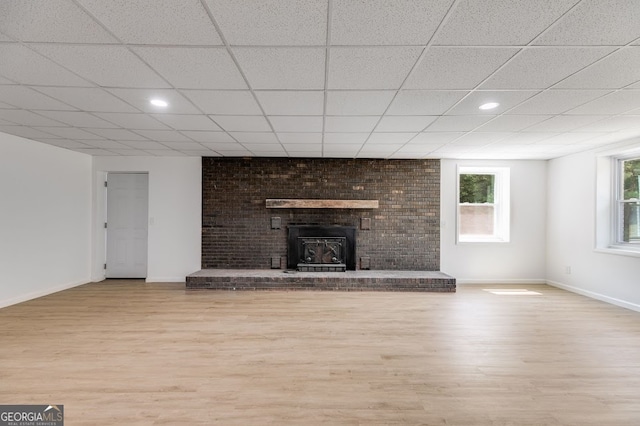 unfurnished living room with light hardwood / wood-style flooring, a drop ceiling, brick wall, and a brick fireplace