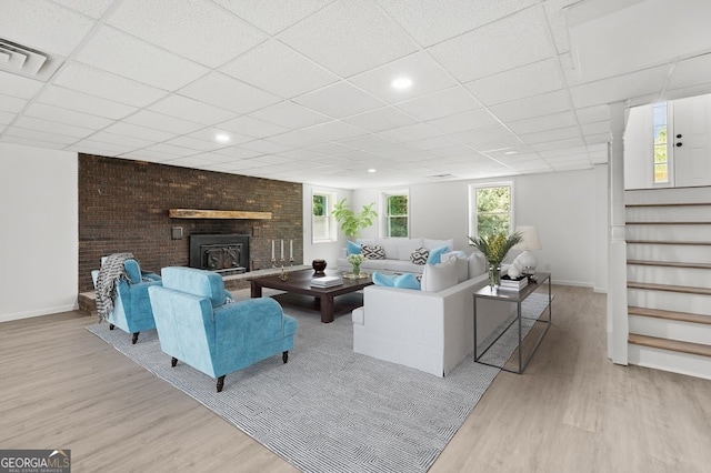 living room featuring brick wall, a fireplace, a paneled ceiling, and light hardwood / wood-style floors