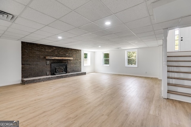 unfurnished living room featuring a drop ceiling, a fireplace, light hardwood / wood-style floors, and brick wall