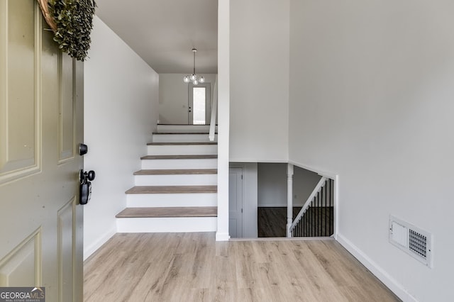 stairs featuring light wood-type flooring and an inviting chandelier