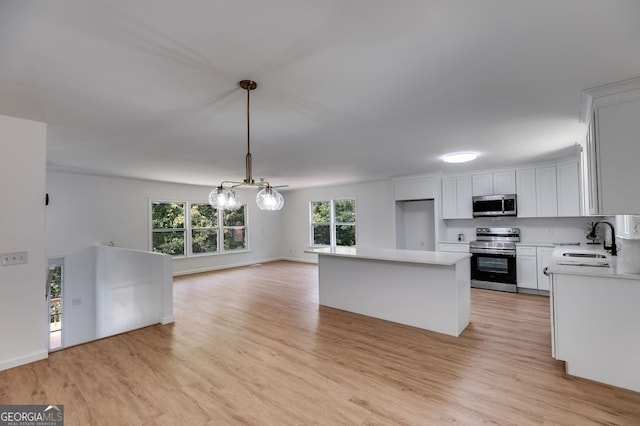 kitchen featuring appliances with stainless steel finishes, a notable chandelier, sink, light hardwood / wood-style flooring, and decorative light fixtures