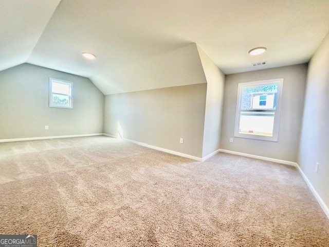 additional living space featuring vaulted ceiling, light colored carpet, and plenty of natural light