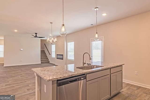 kitchen with dishwasher, sink, light stone counters, a center island with sink, and hardwood / wood-style flooring