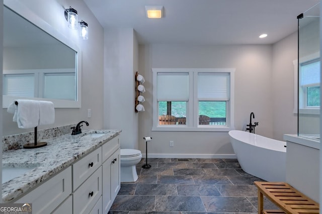 full bathroom featuring a freestanding tub, toilet, a sink, baseboards, and double vanity