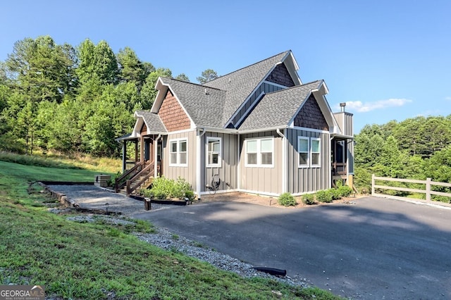 exterior space with driveway, a shingled roof, board and batten siding, and fence