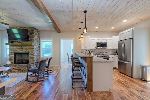 kitchen with stainless steel appliances, hanging light fixtures, light hardwood / wood-style floors, backsplash, and light stone countertops