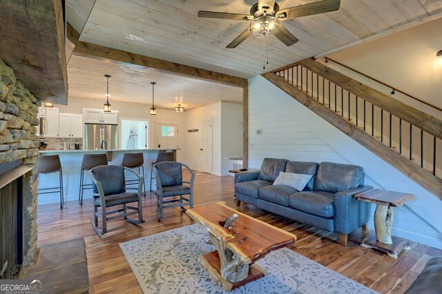 living room with light wood-type flooring, a fireplace, beamed ceiling, ceiling fan, and wood ceiling