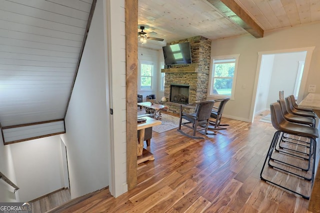 living room with beam ceiling, light hardwood / wood-style flooring, a stone fireplace, and a healthy amount of sunlight