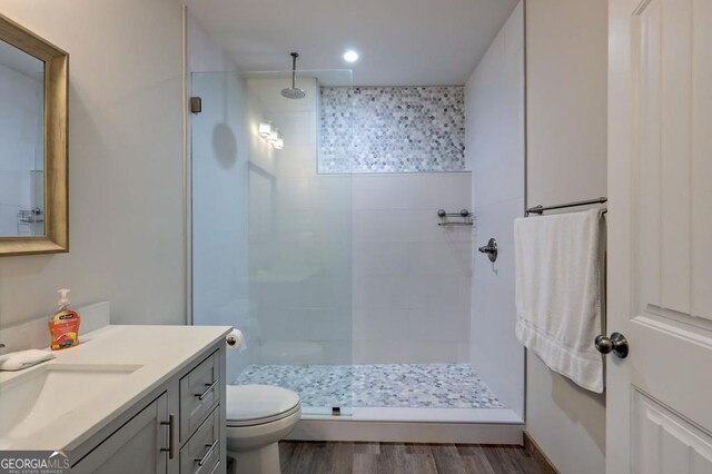 bathroom with hardwood / wood-style floors, tiled shower, vanity, and toilet