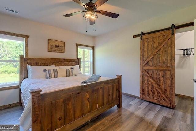 bedroom featuring dark wood-type flooring, a barn door, multiple windows, and visible vents