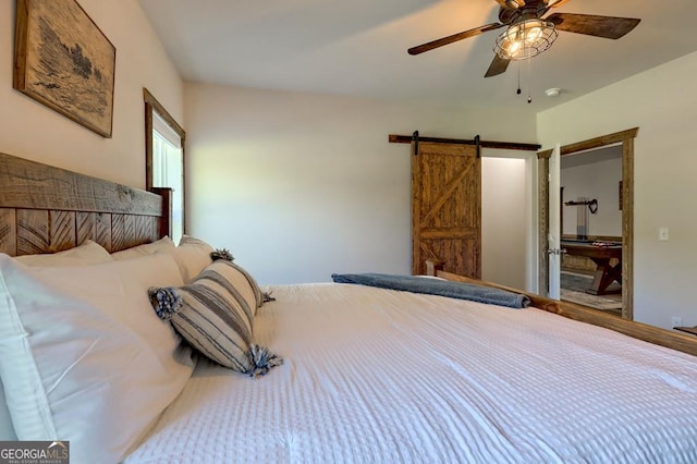 bedroom with a barn door, connected bathroom, and a ceiling fan