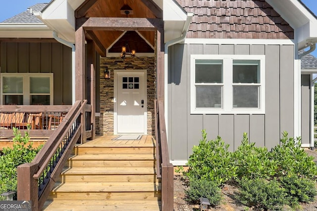 view of exterior entry featuring stone siding, a shingled roof, and board and batten siding