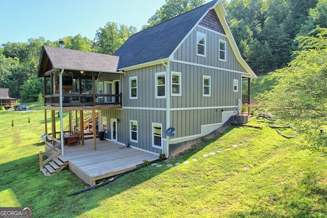 back of house with central AC unit, roof with shingles, a lawn, a wooden deck, and board and batten siding