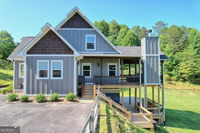 view of front of house featuring covered porch, a shingled roof, a front lawn, board and batten siding, and a chimney