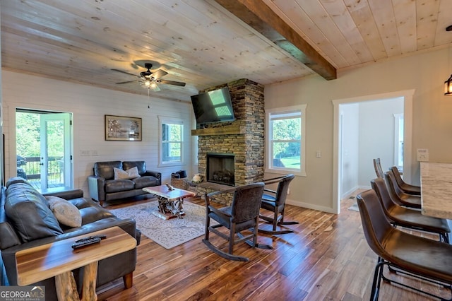 living room with ceiling fan, wood-type flooring, a stone fireplace, and wooden ceiling