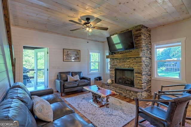 living room with wooden ceiling, ceiling fan, a stone fireplace, and wood finished floors