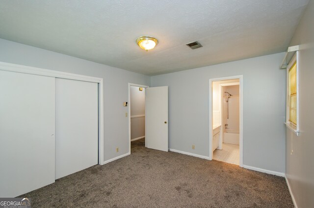 unfurnished bedroom with ensuite bath, a textured ceiling, carpet, and a closet