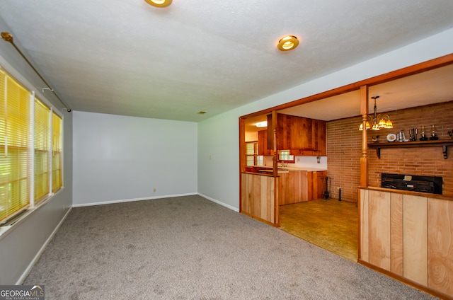 unfurnished living room featuring a notable chandelier, brick wall, and light colored carpet