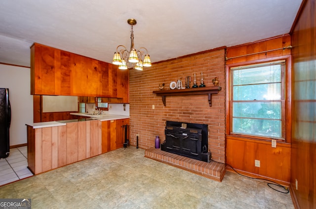 kitchen with a chandelier, kitchen peninsula, a brick fireplace, light tile patterned floors, and decorative light fixtures