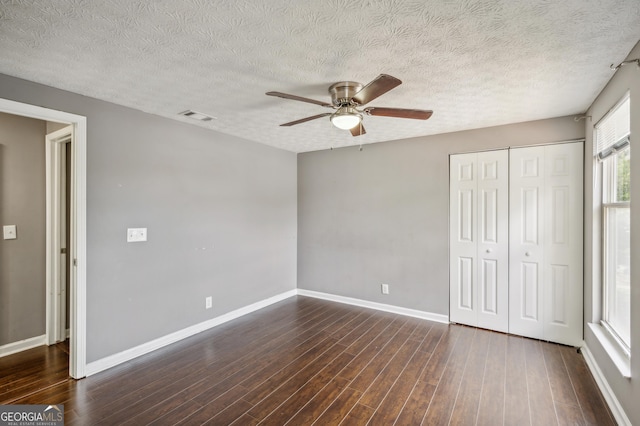 unfurnished bedroom with dark wood-style flooring, a closet, visible vents, and baseboards