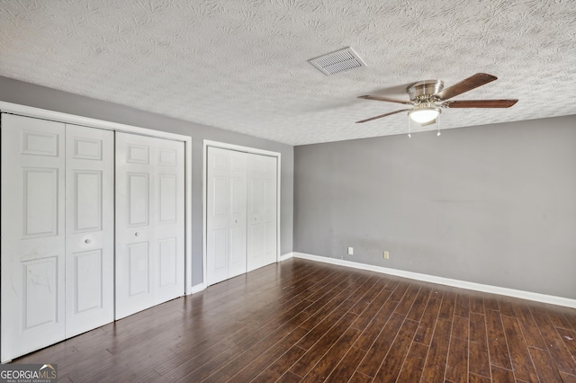 unfurnished bedroom with baseboards, dark wood-type flooring, visible vents, and multiple closets