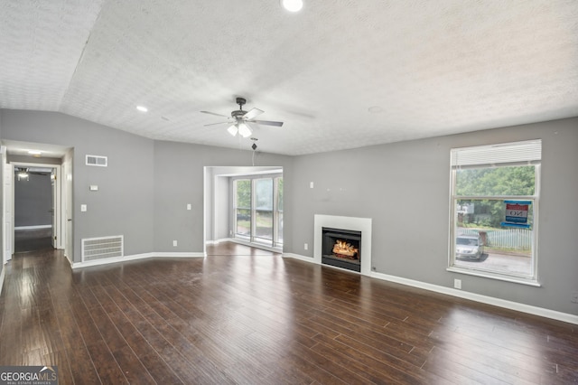 unfurnished living room with lofted ceiling, a warm lit fireplace, visible vents, and dark wood-style flooring