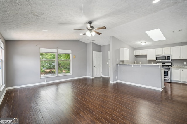 unfurnished living room featuring lofted ceiling with skylight, dark wood finished floors, baseboards, and a ceiling fan