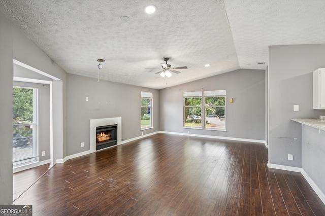 unfurnished living room featuring dark wood-type flooring, vaulted ceiling, ceiling fan, a lit fireplace, and baseboards