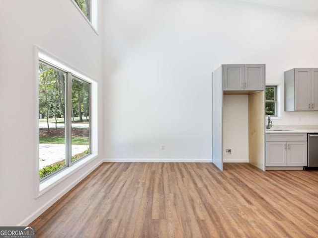 unfurnished living room with a wealth of natural light, sink, a towering ceiling, and light wood-type flooring