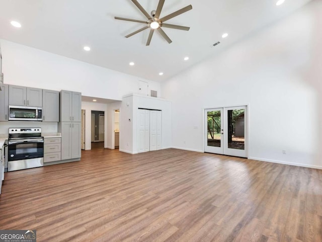 unfurnished living room with ceiling fan, french doors, a towering ceiling, and light wood-type flooring