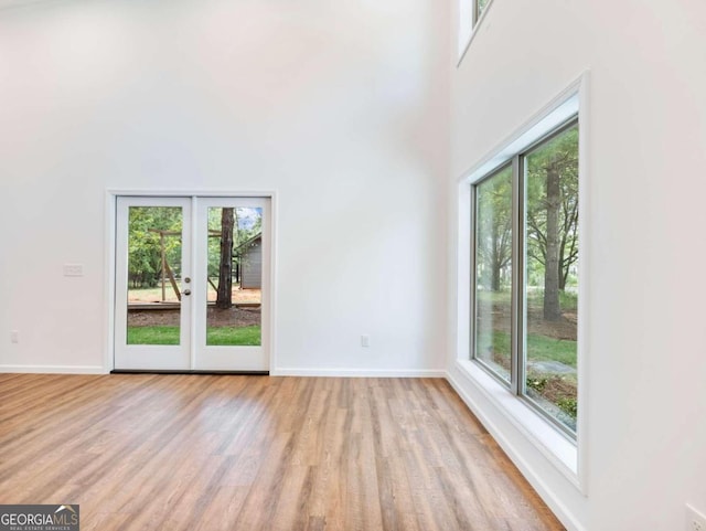 empty room with plenty of natural light, a towering ceiling, french doors, and light hardwood / wood-style flooring