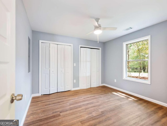 unfurnished bedroom featuring light wood-type flooring, ceiling fan, and multiple closets