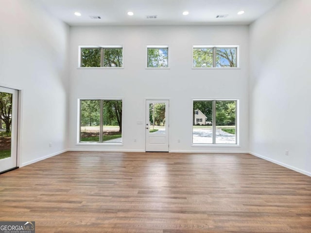 unfurnished living room featuring plenty of natural light, a towering ceiling, and light hardwood / wood-style flooring