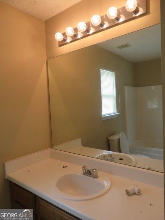 bathroom with vanity, a shower, a textured ceiling, and toilet