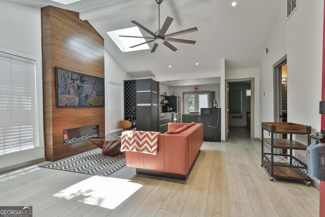 living room with high vaulted ceiling, wooden walls, light hardwood / wood-style floors, a skylight, and ceiling fan