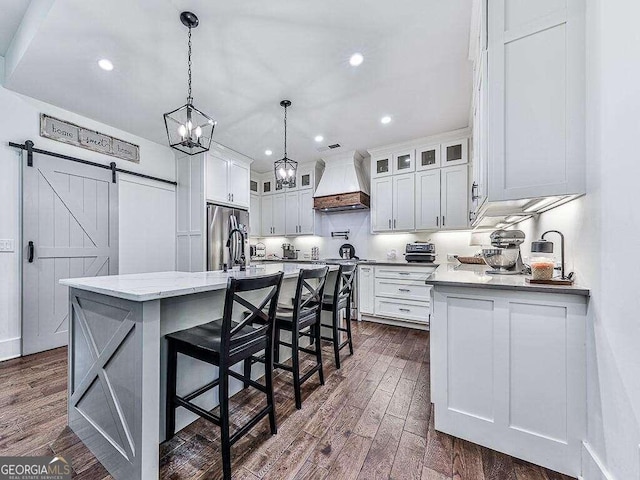 kitchen featuring stainless steel appliances, white cabinetry, custom range hood, dark wood-type flooring, and a barn door