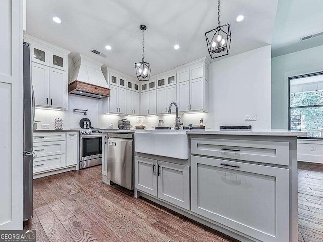 kitchen featuring dark wood-type flooring, stainless steel appliances, pendant lighting, and premium range hood