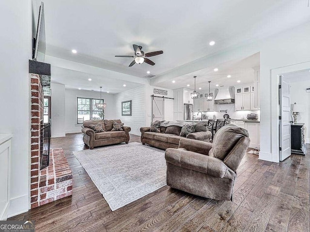 living room with ceiling fan, a barn door, dark wood-type flooring, and sink