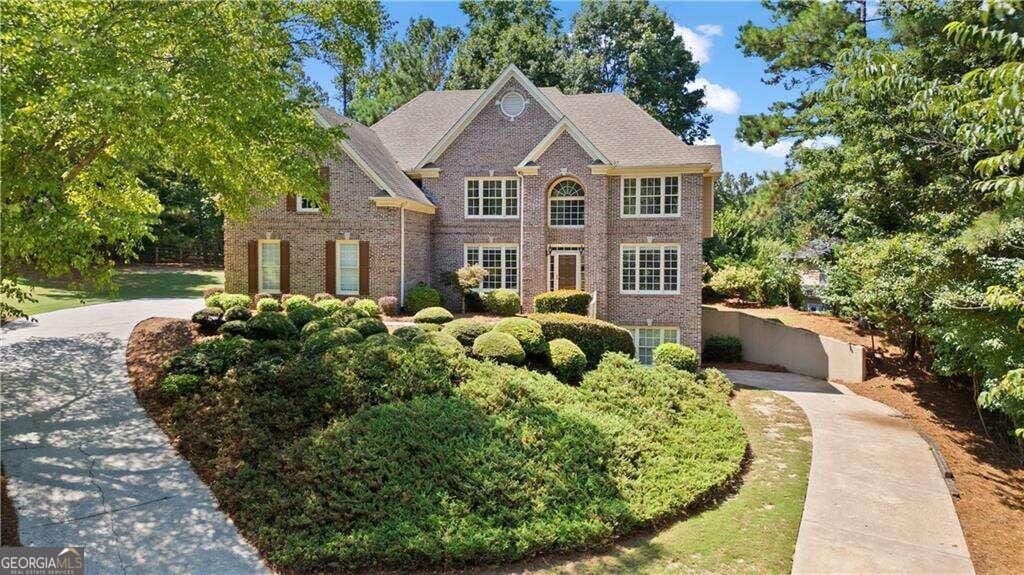 view of front facade with driveway, fence, and brick siding