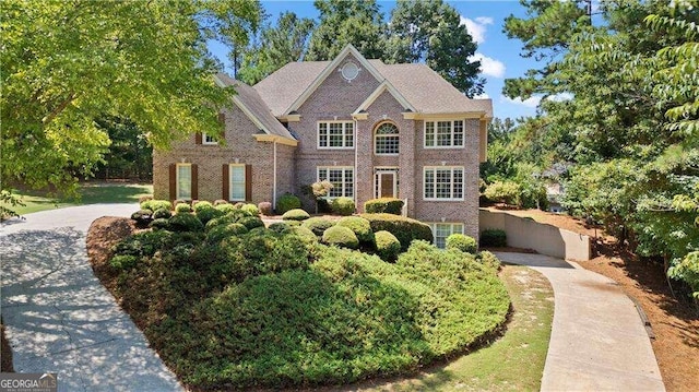 view of front facade with driveway, fence, and brick siding