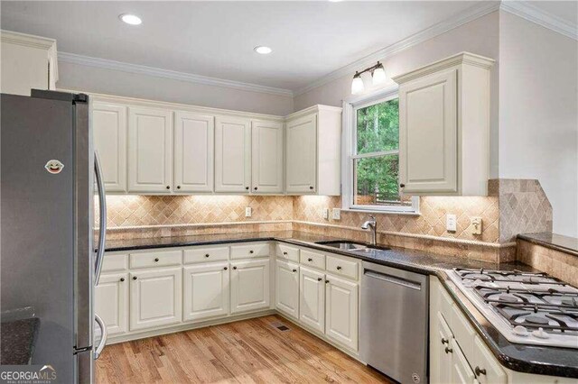 kitchen with decorative backsplash, appliances with stainless steel finishes, sink, ornamental molding, and light hardwood / wood-style floors