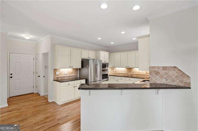 kitchen featuring appliances with stainless steel finishes, kitchen peninsula, dark stone countertops, light hardwood / wood-style floors, and tasteful backsplash