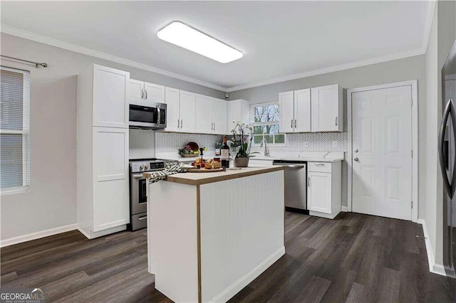 kitchen with white cabinetry, ornamental molding, appliances with stainless steel finishes, and a kitchen island