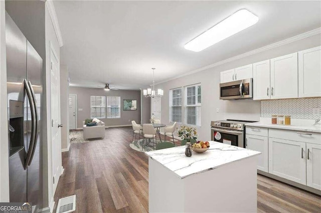 kitchen with appliances with stainless steel finishes, a kitchen island, dark wood-type flooring, white cabinets, and tasteful backsplash