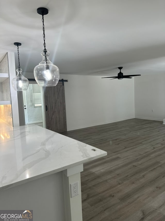 unfurnished dining area with ceiling fan, a barn door, and dark wood-type flooring