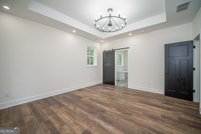 unfurnished bedroom with a notable chandelier, a barn door, a raised ceiling, and dark wood-type flooring