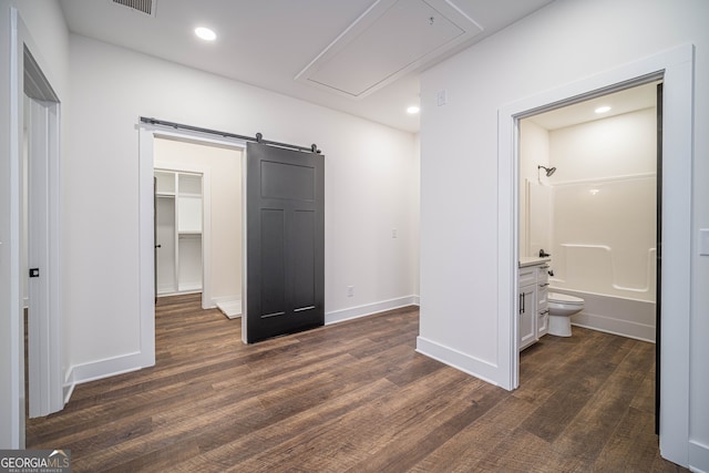 unfurnished bedroom with connected bathroom, a barn door, a walk in closet, and dark hardwood / wood-style flooring