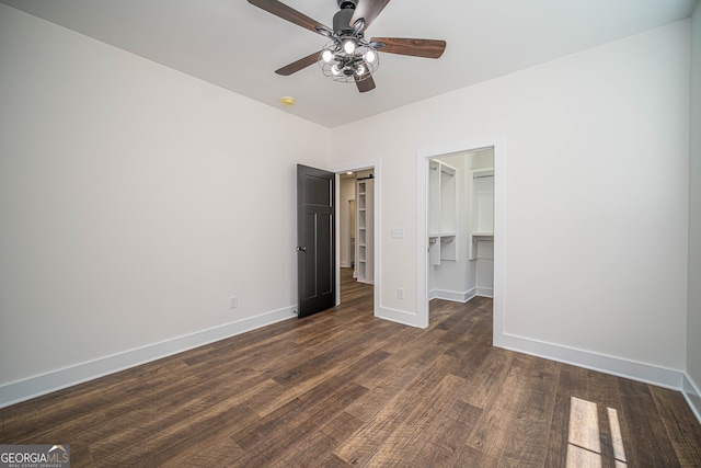 unfurnished bedroom featuring a walk in closet, ceiling fan, a closet, and dark wood-type flooring