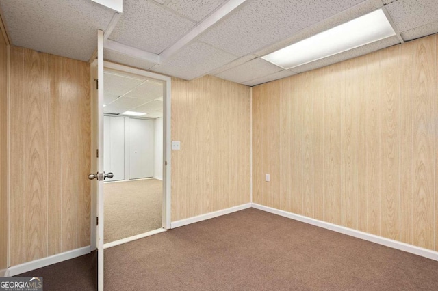 unfurnished bedroom with carpet flooring, a drop ceiling, and wooden walls