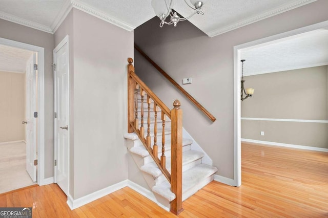 stairs featuring a notable chandelier, a textured ceiling, ornamental molding, and wood-type flooring